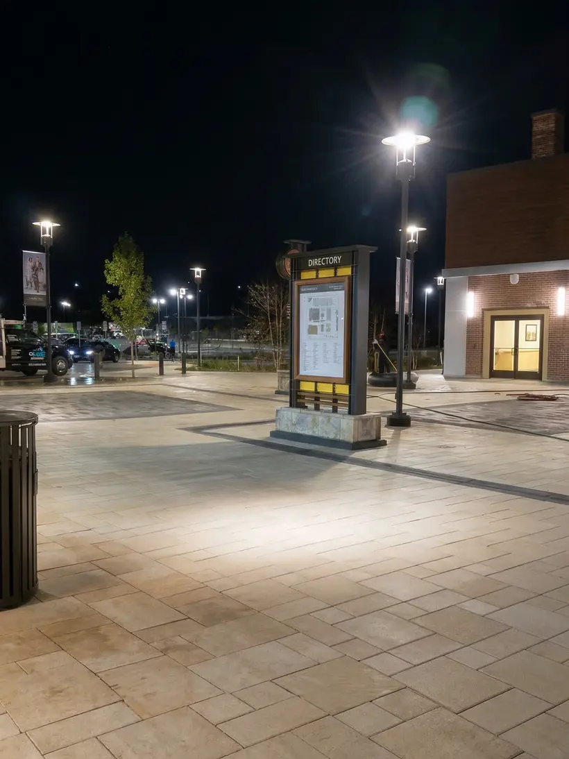 Plaza nocturna con t&oacute;tem direccional y postes de luz