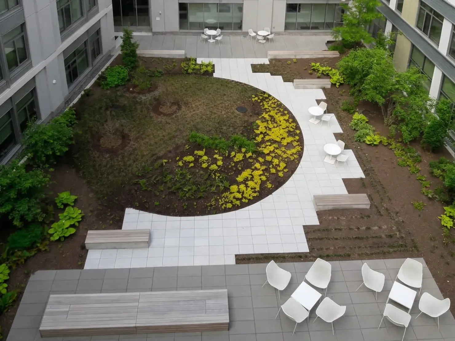 Patio-jardín terminado visto desde arriba: césped circular, plaza de adoquín y camas plantadas impecables